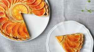 A baked orange pie, on a white porcliean plate, with a less than a quarter missing, The miissng slice is a on smaller white plate, next to it.